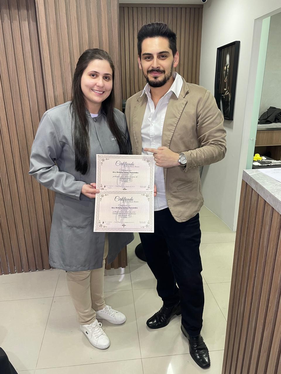 Dr. Lopez ao lado de aluna segurando dois certificados da formação presencial